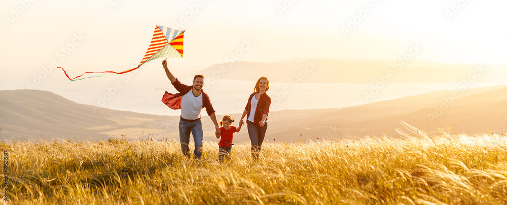 幸福的家庭父亲、母亲和孩子的女儿在日落时在大自然上放风筝