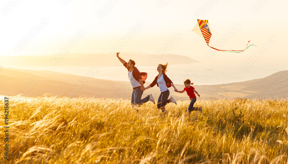 幸福的家庭父亲、母亲和孩子的女儿在日落时在大自然上放风筝