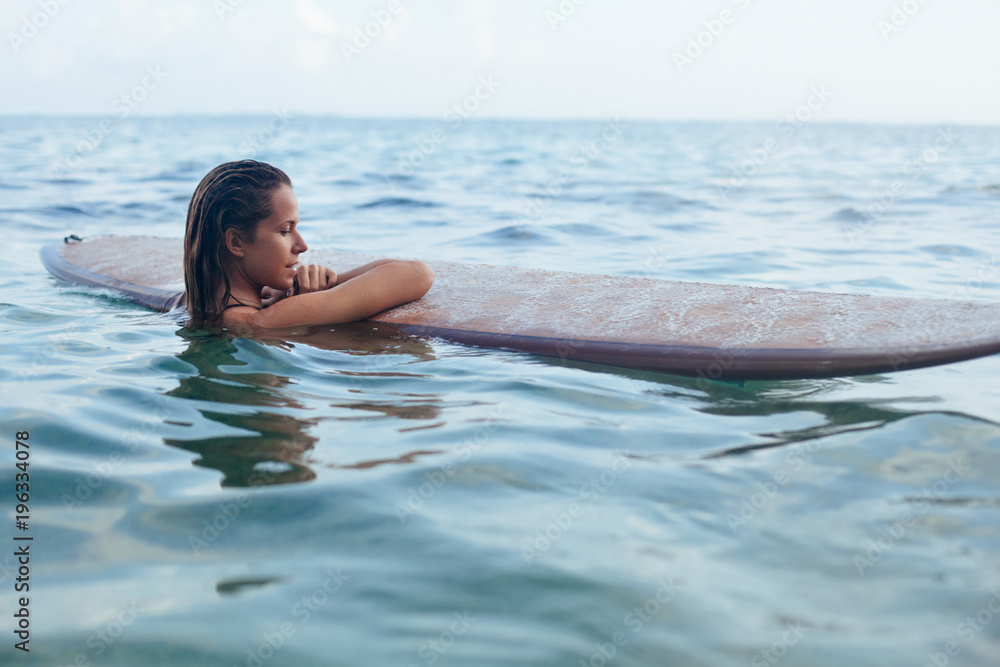 快乐的女人在冲浪前玩得很开心。冲浪女孩拿着冲浪板，看着日落的天空。人们在