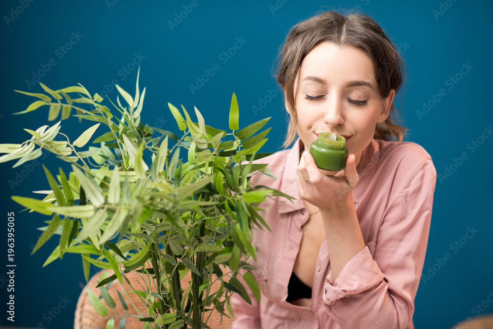 一位年轻微笑的女士与绿色植物坐在蓝色墙壁上享受芳香奶油的肖像