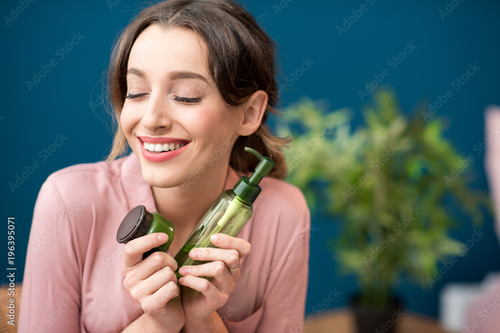 一位年轻女子的画像，家中蓝色墙壁背景上拿着装有乳液的绿色瓶子