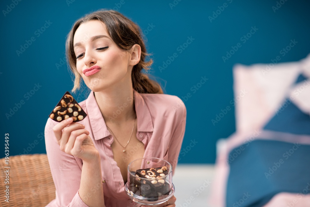美丽的女人坐在室内蓝色墙壁背景上享受巧克力