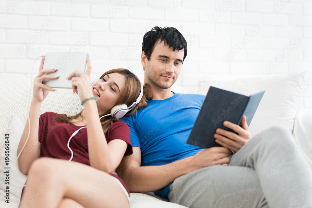一对年轻夫妇在家里客厅的沙发上放松。听音乐，读博