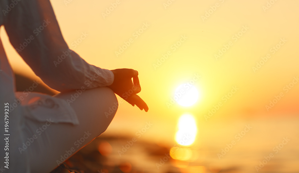 日落时在海滩上做瑜伽冥想的女人的手