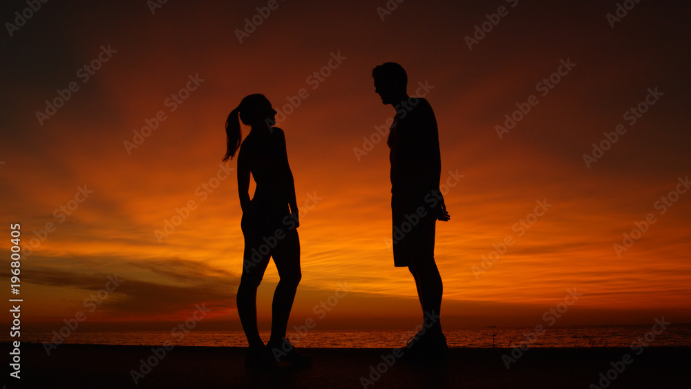 低角度：橙色日出时，男朋友和女朋友在海滩上聊天。