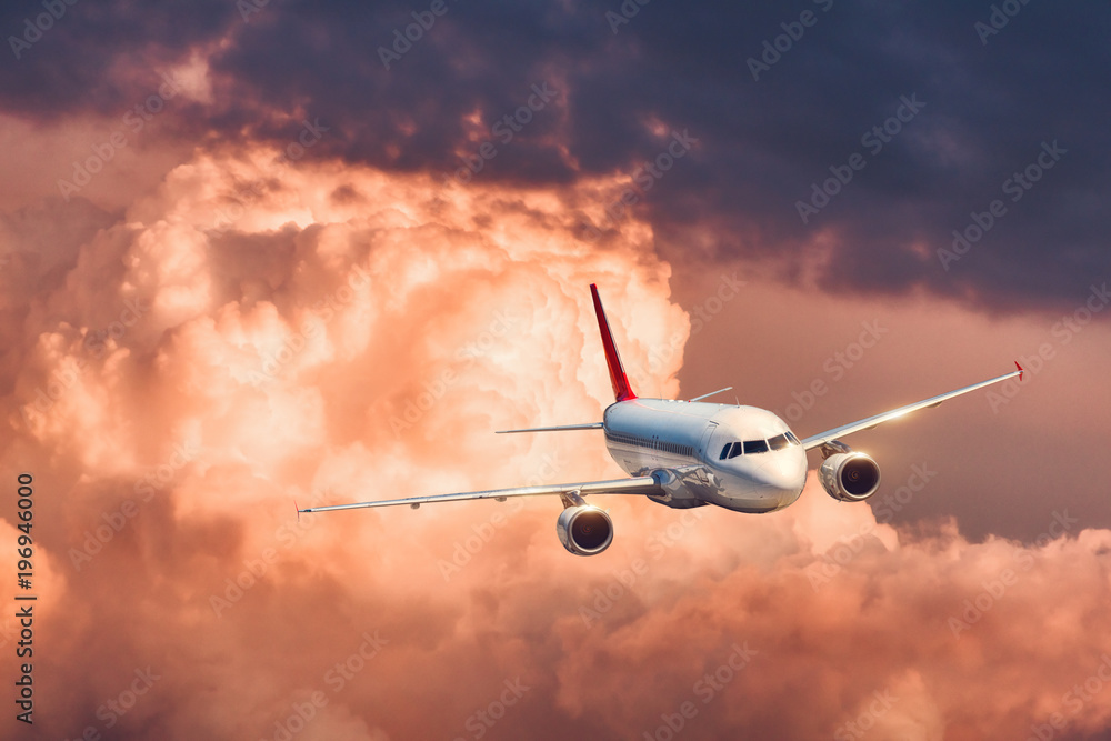 美丽的飞机在五颜六色的日落下低云飞行。白色客机的场景