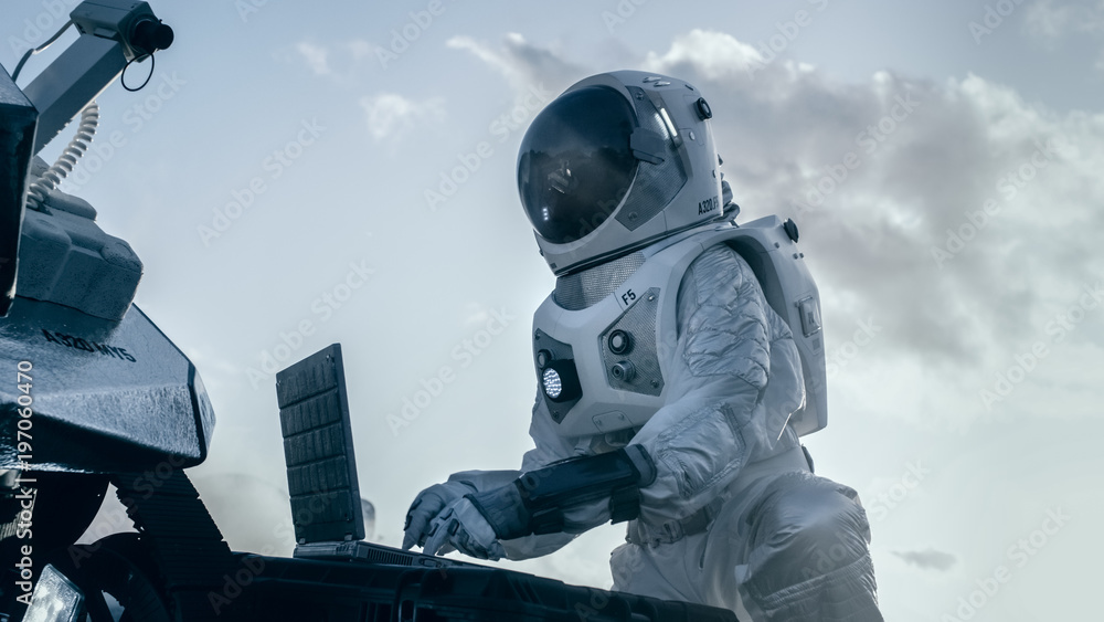 穿着太空服的宇航员在笔记本电脑上工作，在一颗新的外星星球上调整漫游者。天光高-T