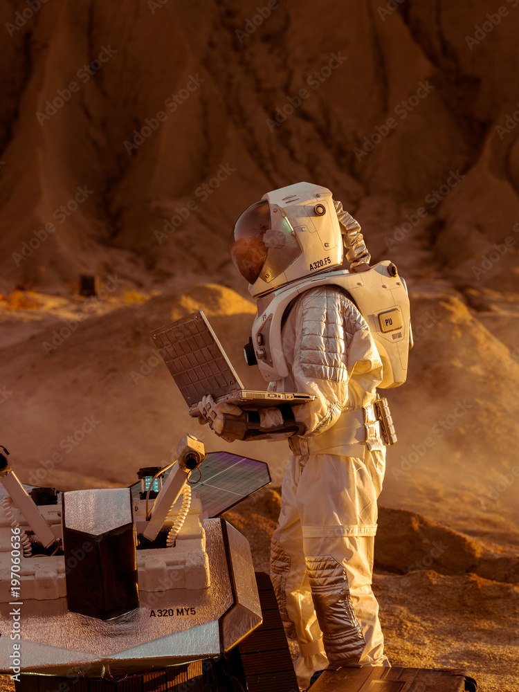 穿着太空服的宇航员在笔记本电脑上工作，为火星的进一步探索调整漫游者。太空