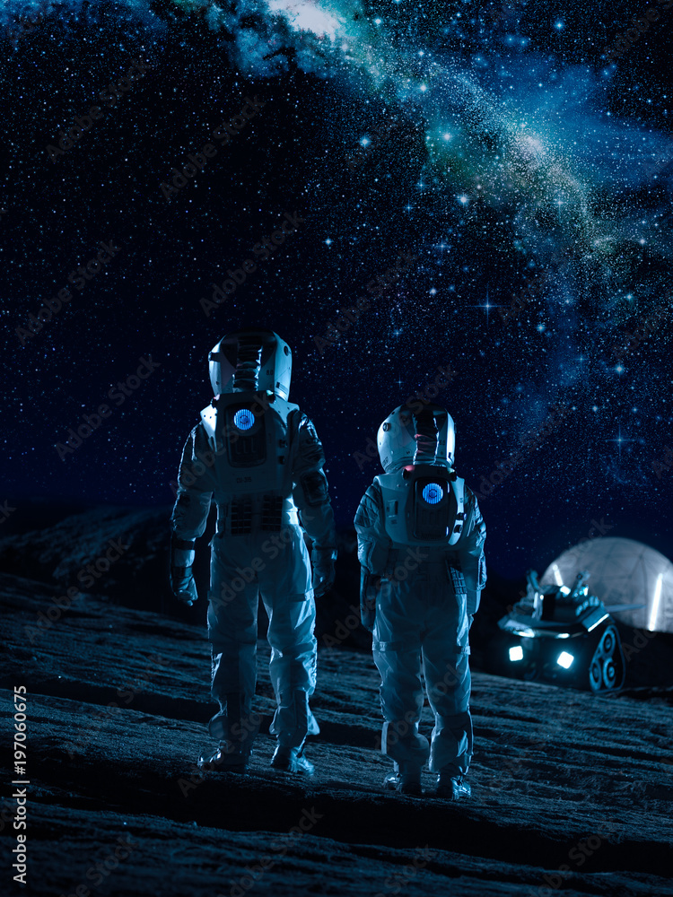 两名身穿太空服的宇航员站在外星行星上看着银河系中的恒星。S