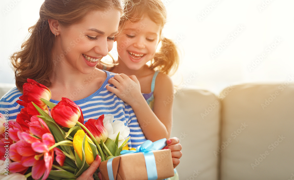 happy mothers day! child daughter   gives mother a bouquet of flowers to tulips and gift