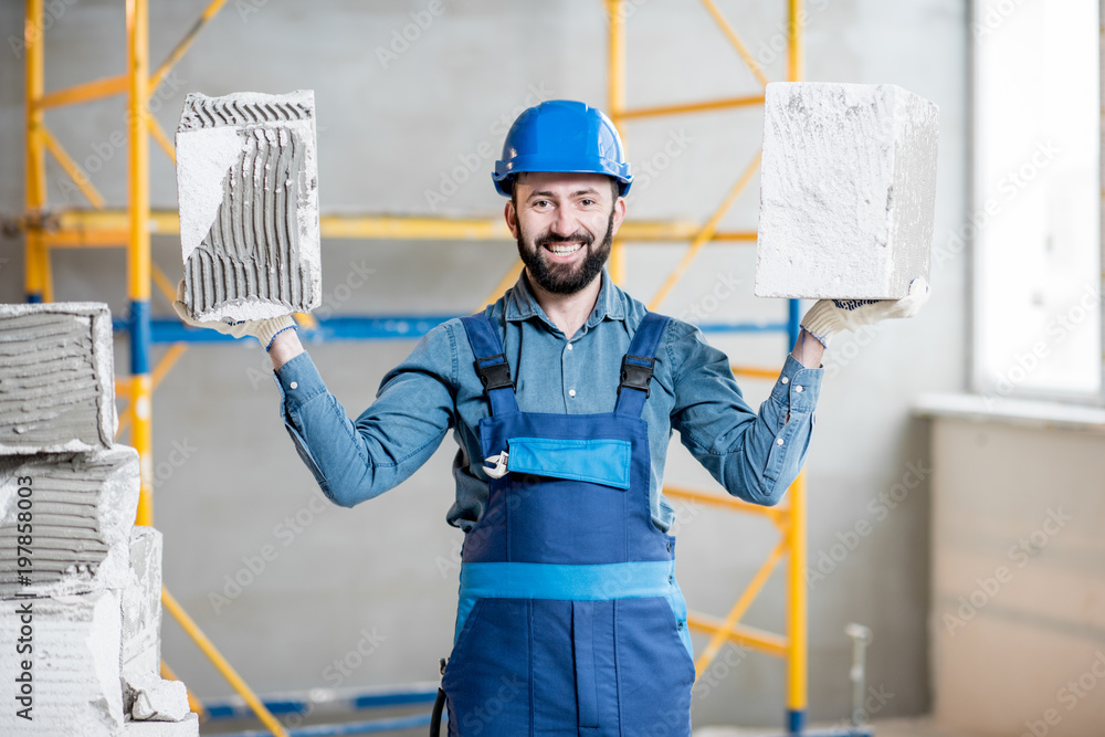 一位强壮的建筑工人在室内建筑工地上穿着统一的积木的肖像