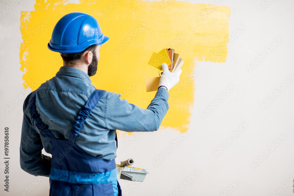 穿着蓝色工作服的画家将黄色墙壁与室内的色板进行比较