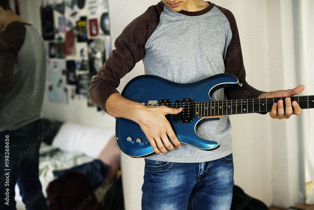 十几岁的男孩在卧室里弹电吉他的爱好和音乐概念