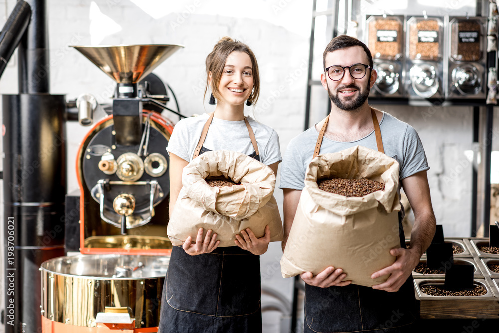 两位穿着制服的快乐咖啡师拿着装满咖啡豆的袋子站在咖啡馆的肖像