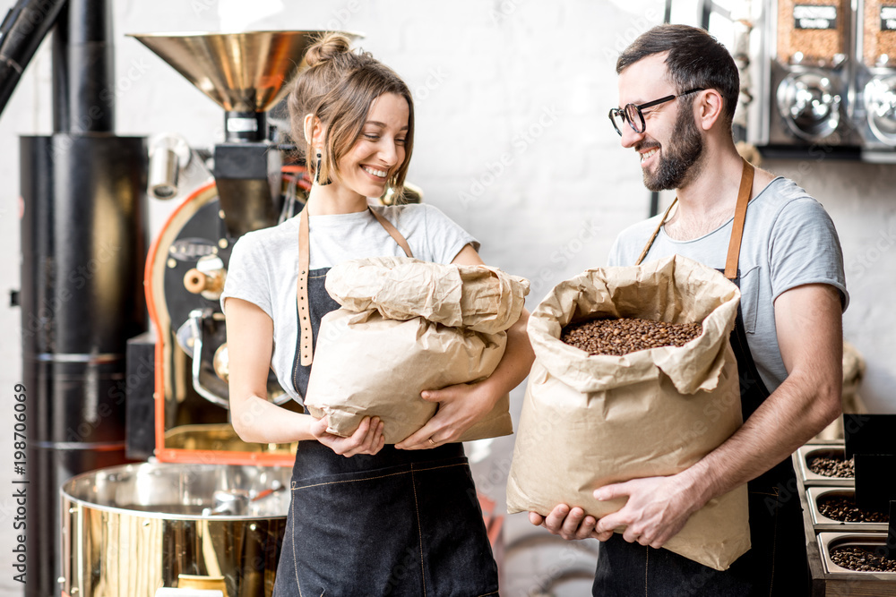两位穿着制服的快乐咖啡师拿着装满咖啡豆的袋子站在咖啡馆的肖像