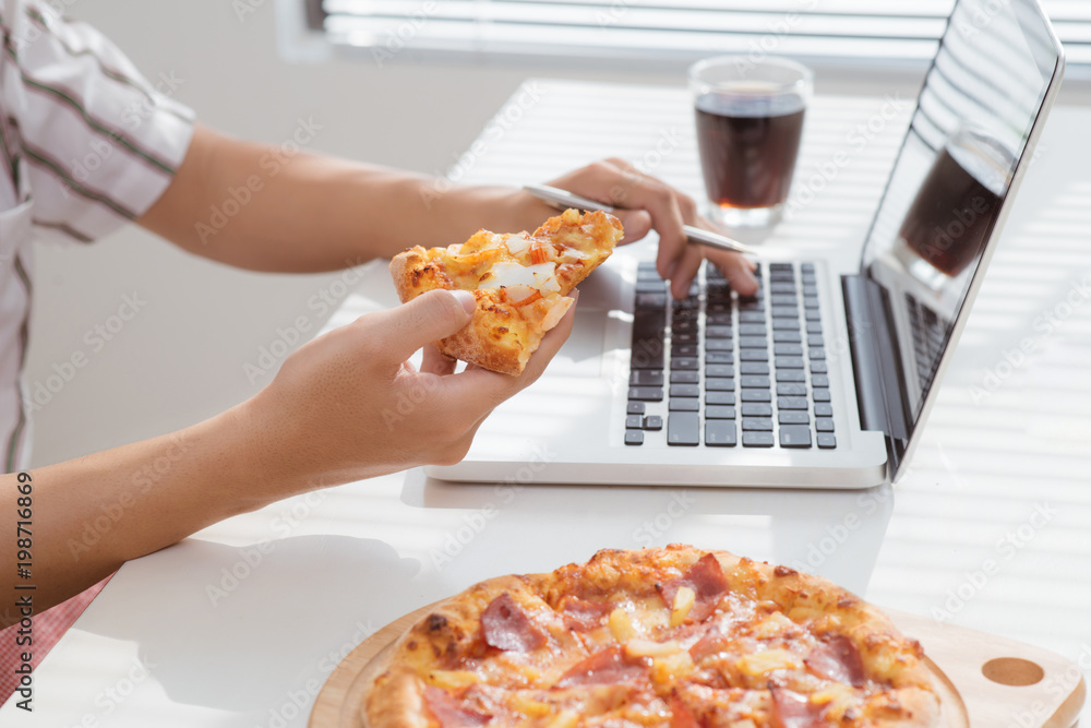 一名男子在笔记本电脑上工作时用手吃披萨