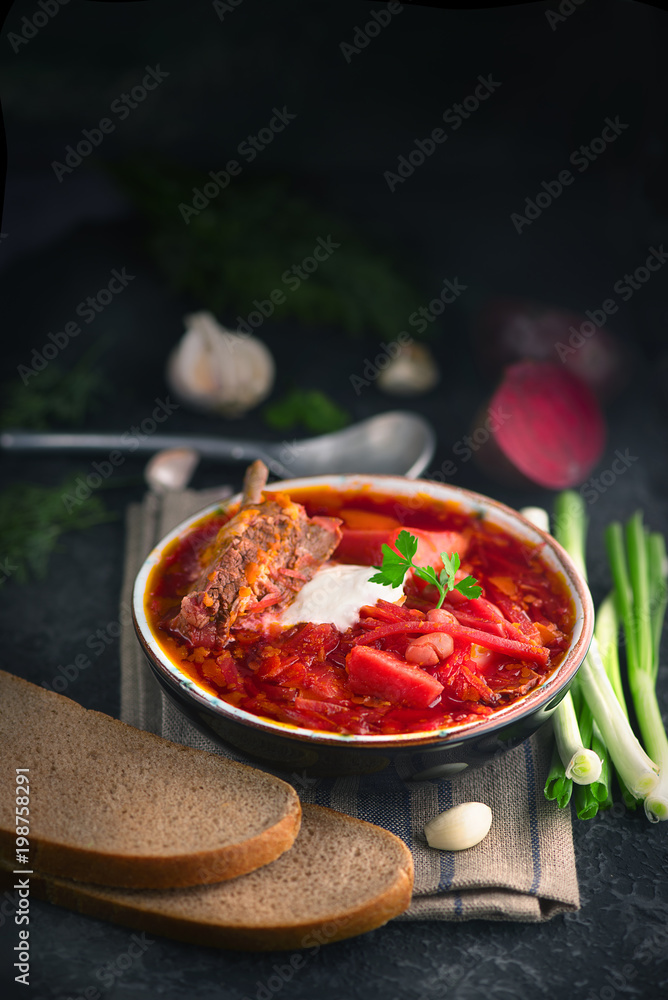 Traditional Ukrainian russian borscht. Plate of red beet root soup borsch on black rustic table. Bee