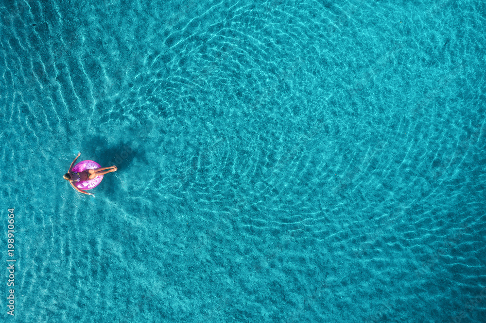 蓝色L，透明绿松石海中，年轻女子在粉色游泳圈上游泳的鸟瞰图