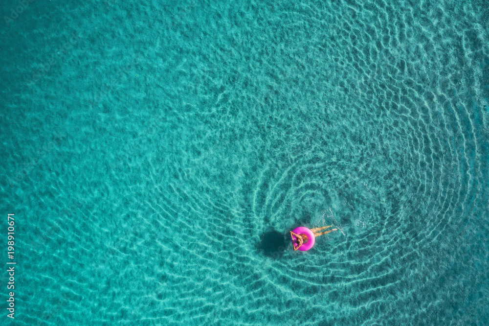 蓝色L，透明绿松石海中，年轻女子在粉色游泳圈上游泳的鸟瞰图