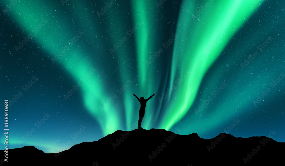 极光和站在挪威山上举起双臂的女人的侧影。极光北方