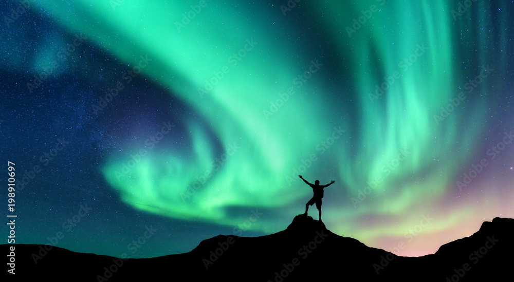 极光和挪威山上举起双臂的站立男子的侧影。北极光