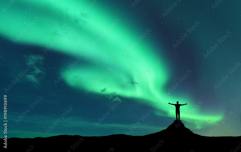 极光和挪威山上举起双臂的站立男子的侧影。北极光