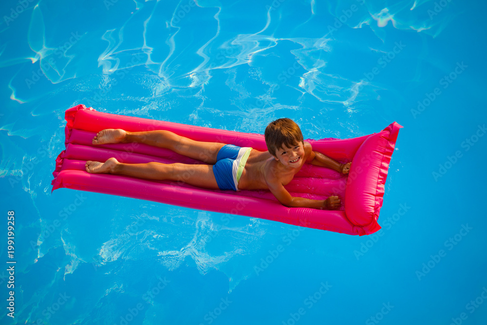 微笑的男孩在粉色充气床垫上游泳