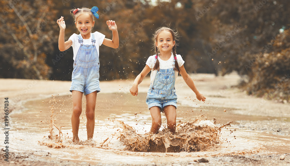 快乐有趣的姐妹双胞胎小女孩穿着橡胶靴在水坑上跳。