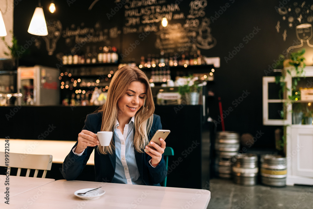 Charming woman using phone while holding a cup of coffee.