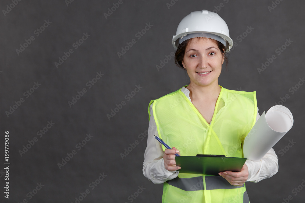 年轻的女工程师戴着防护帽和背心，带着项目。在平板电脑上做笔记