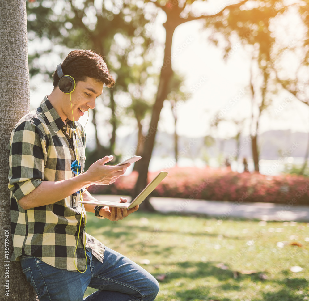 一名男学生坐在城市公园的草地上放松并听音乐