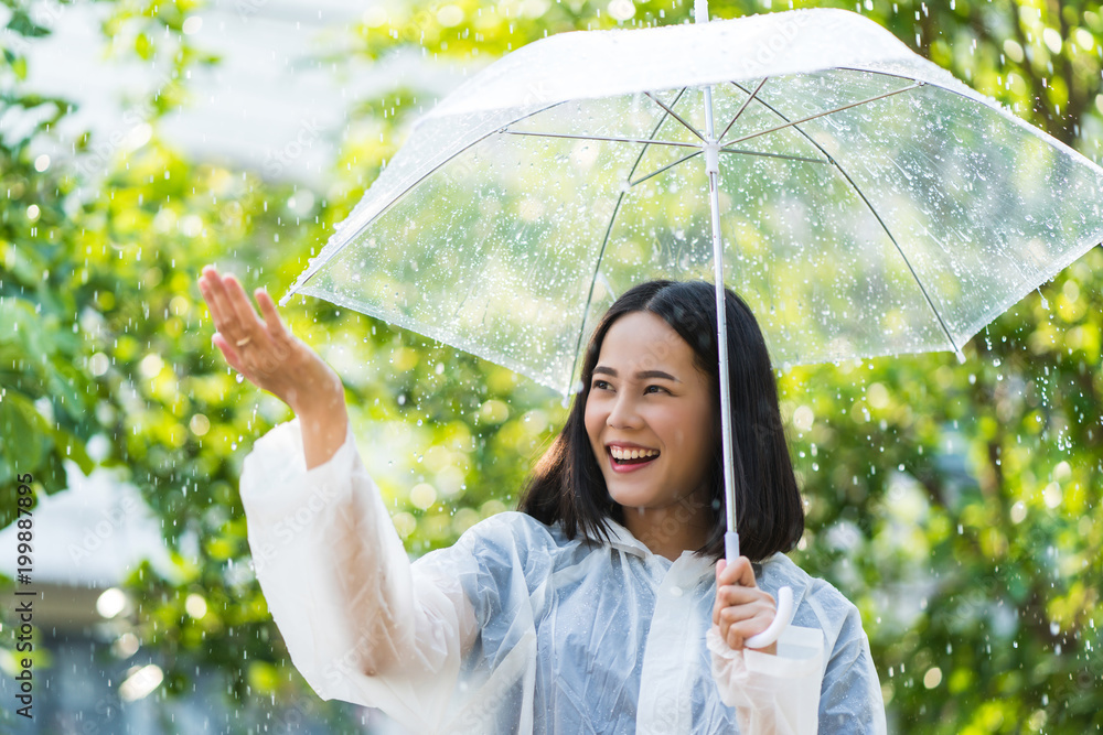 雨天，一位亚洲女士在户外穿着雨衣。她很开心。她用手触摸了雨水。