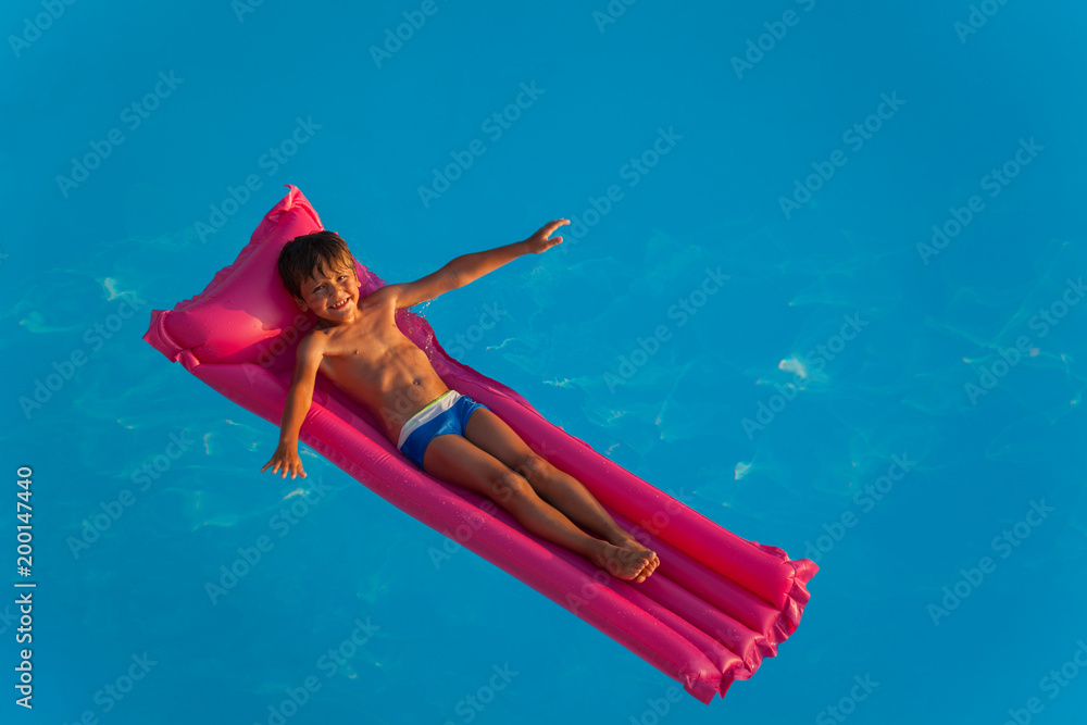 Happy boy relaxing on inflatable mattress in pool