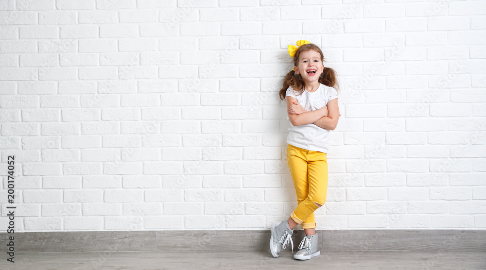 一个空砖墙附近快乐有趣的小女孩。