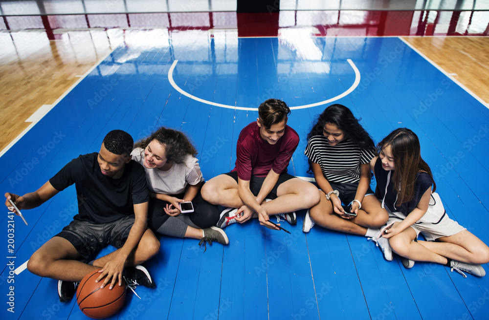 一群年轻的青少年朋友在篮球场上放松并使用智能手机