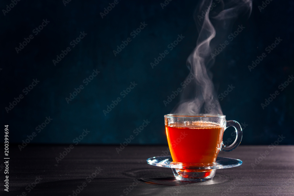 在透明玻璃杯中新鲜冲泡的红茶，蒸汽逸出，背景较暗。