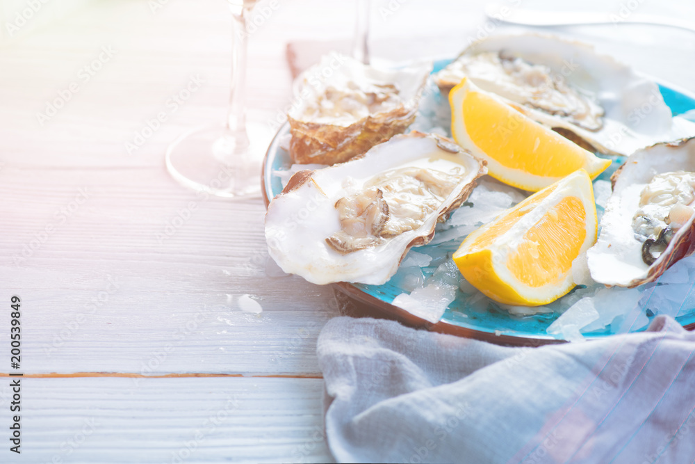 新鲜牡蛎特写在蓝色盘子上，桌上有牡蛎、柠檬和冰。健康的海鲜。牡蛎