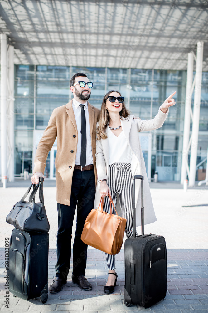 商务旅行中，一对穿着外套的商务情侣拿着行李站在机场附近