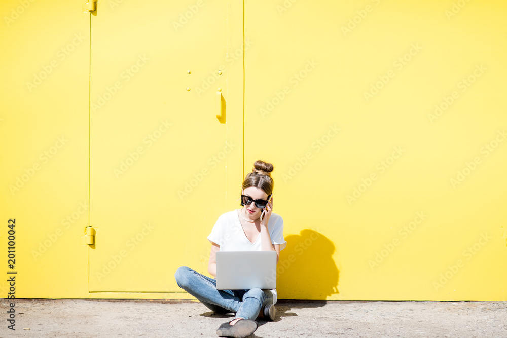 在黄色墙壁背景上用笔记本电脑工作的女人