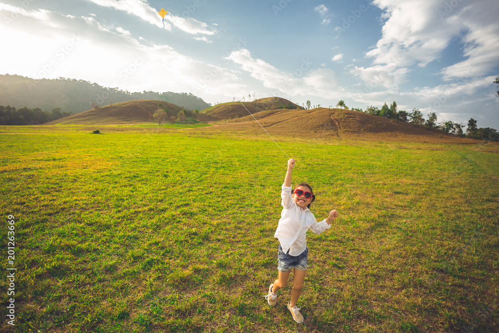 小女孩带着风筝在夏日田野上快乐微笑地奔跑