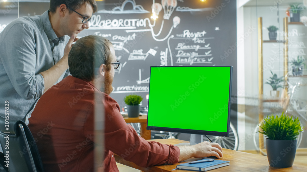 两位男性开发人员谈论项目，而个人电脑有绿色实体屏幕。他们工作