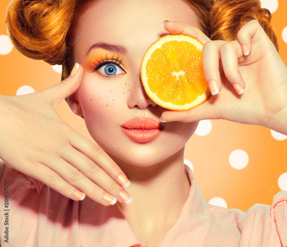 美丽快乐的少女吃多汁的橙子。有雀斑的少女模特，滑稽的红色发型，