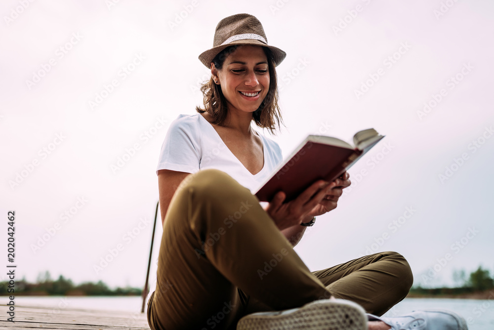 微笑的年轻女士坐在水边看书。
