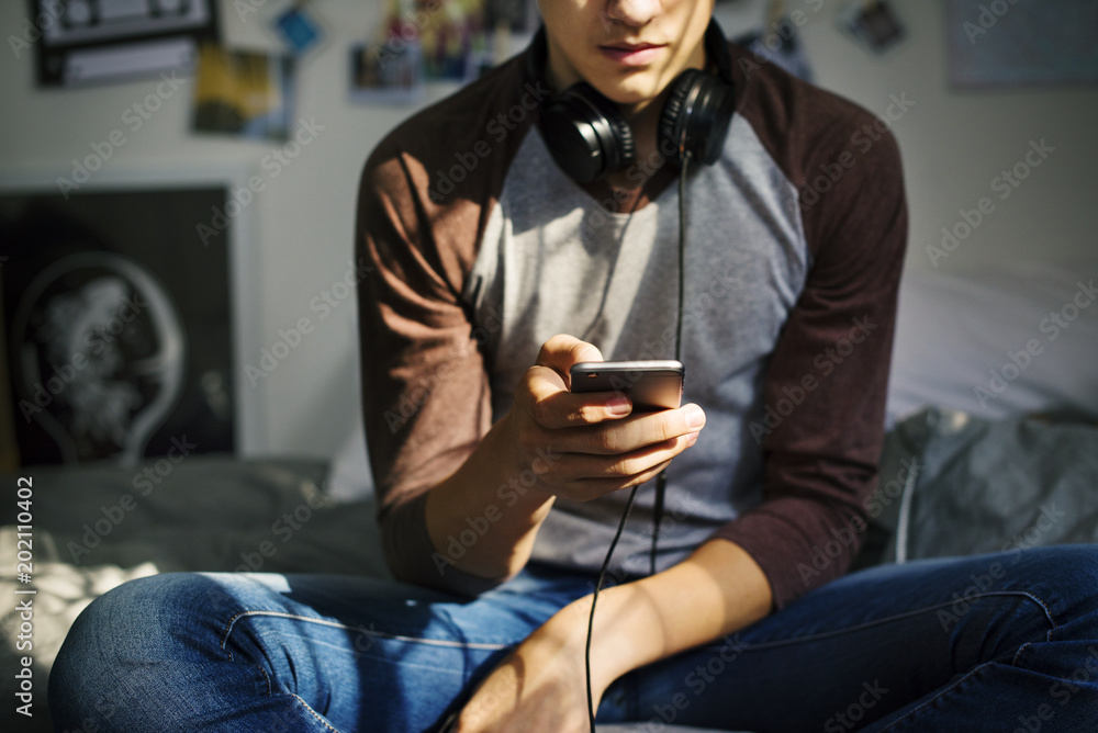 十几岁的男孩在卧室里通过智能手机听音乐