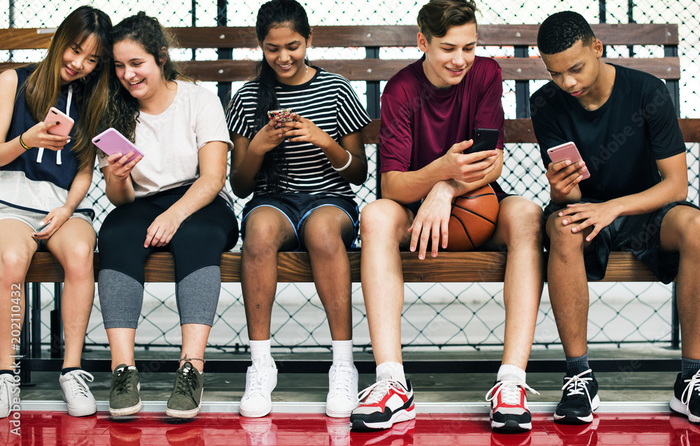 一群年轻的青少年朋友在篮球场上用智能手机放松