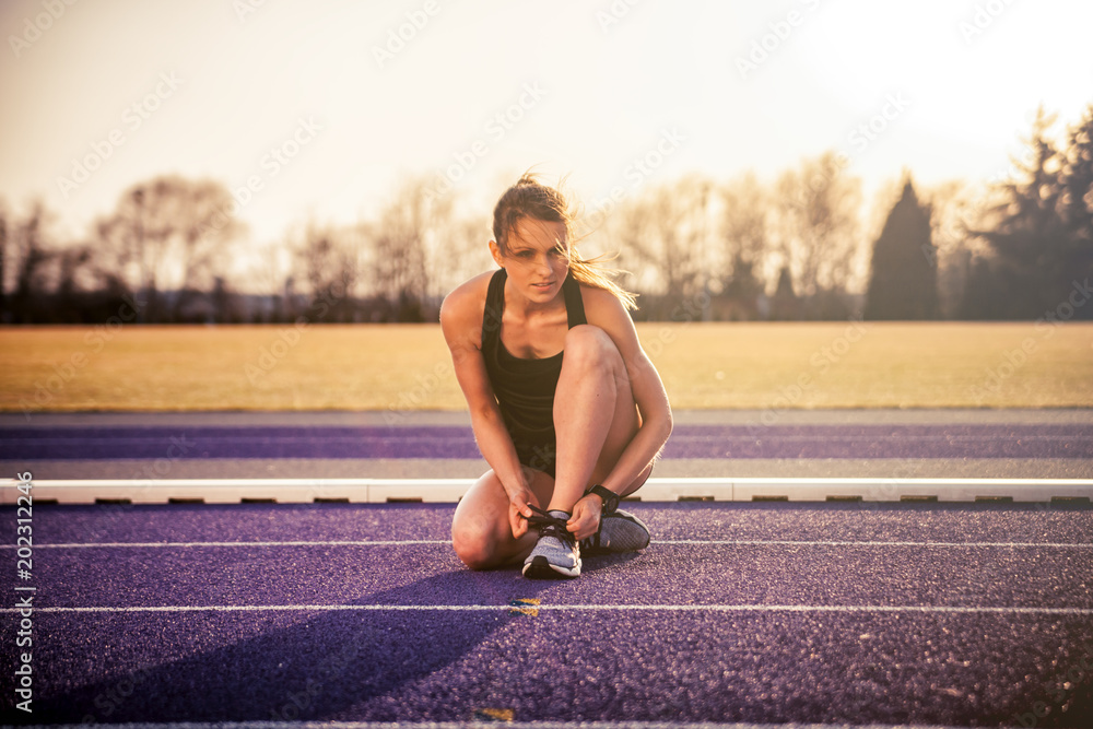 日落时，健身女士在体育场跑道上准备鞋子