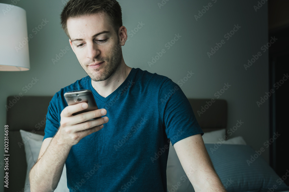 英俊的高加索男子在晨光中用智能手机联系卧室里的人