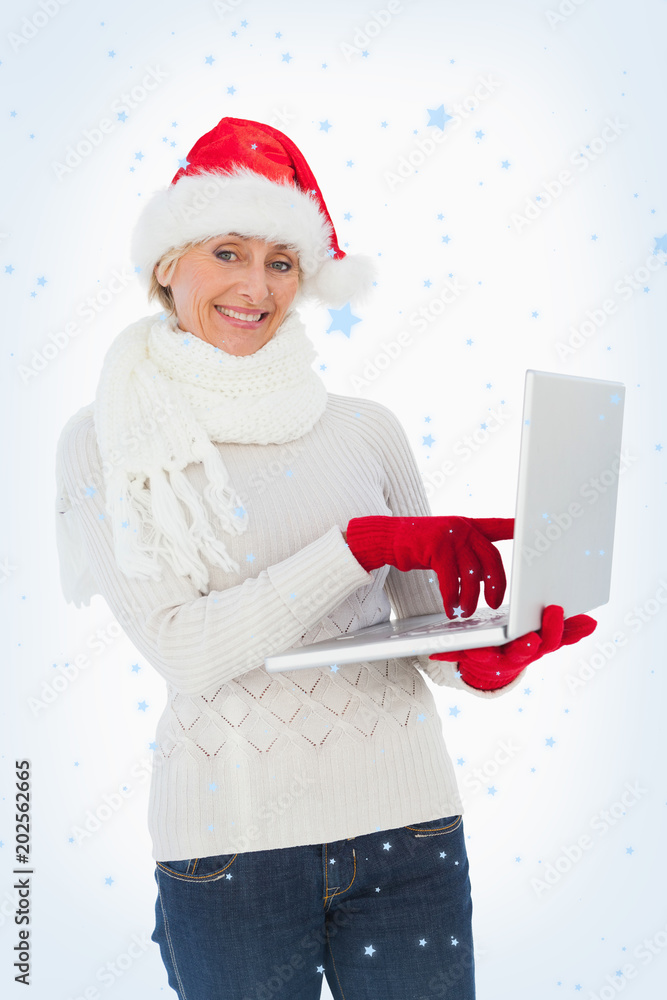节日女性用笔记本电脑对着镜头微笑，抵御降雪