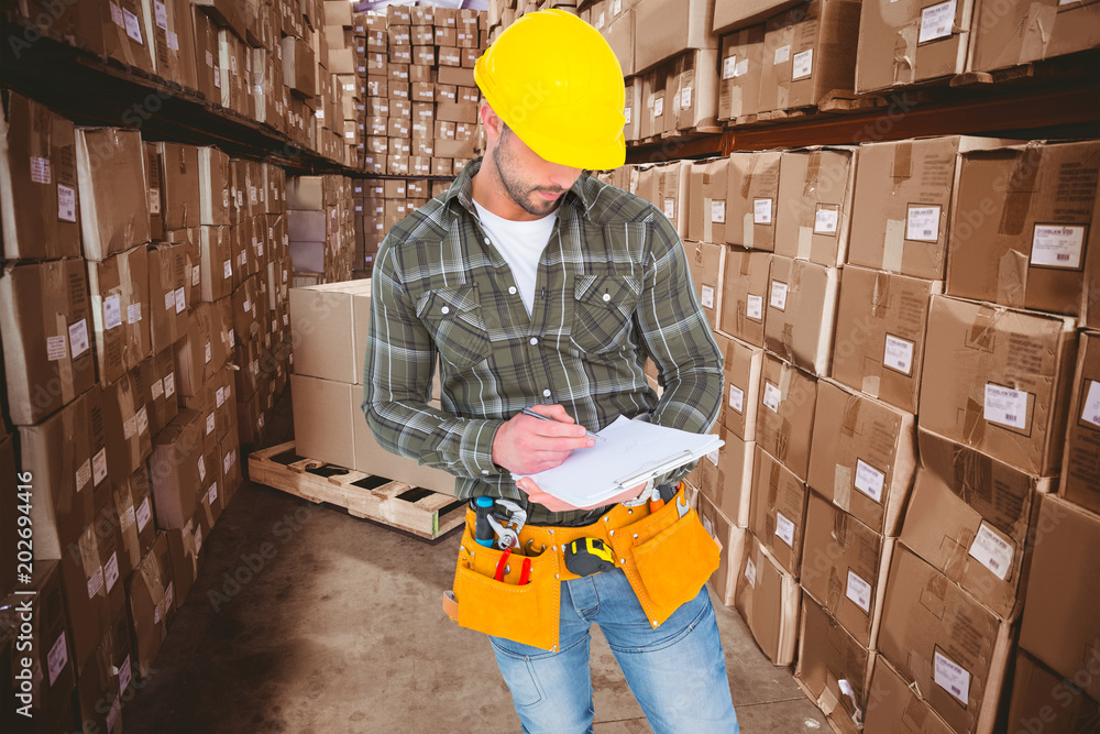 Manual worker writing on clipboard against boxes in warehouse 