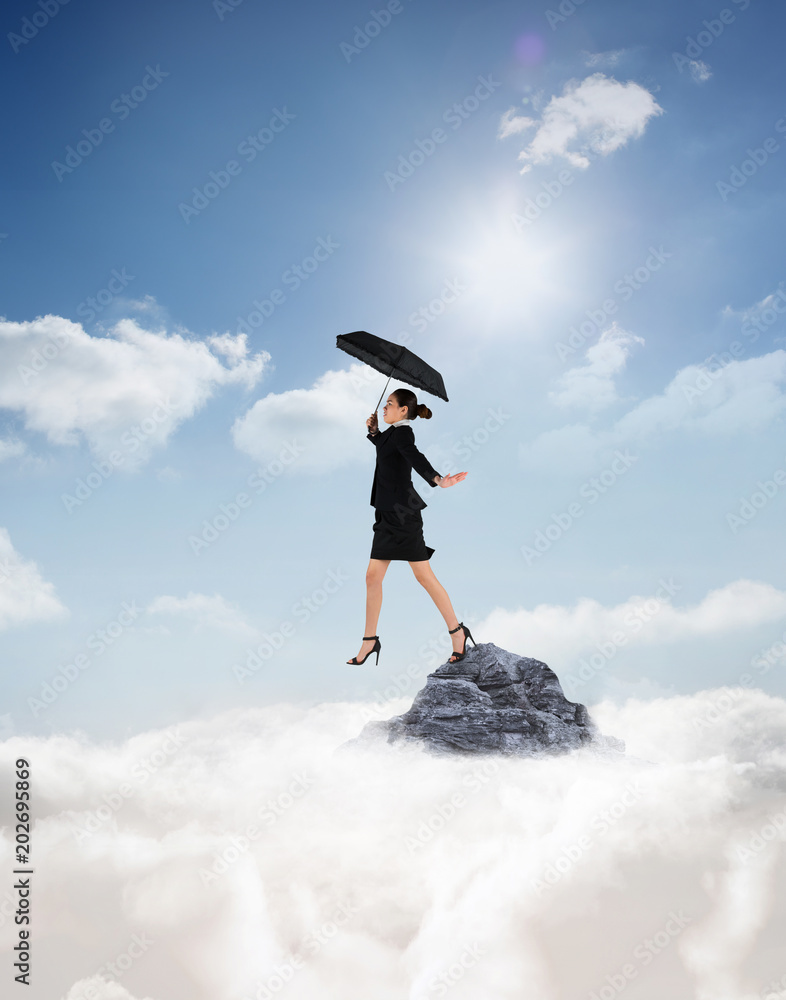 年轻的女商人撑着伞穿过云层对抗山峰